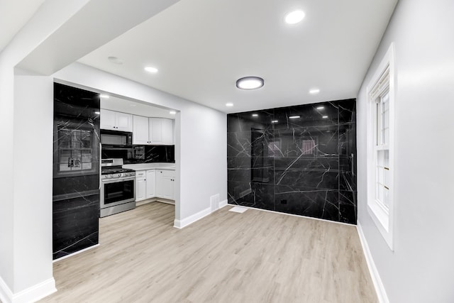 kitchen with tasteful backsplash, black appliances, white cabinets, and light wood-type flooring