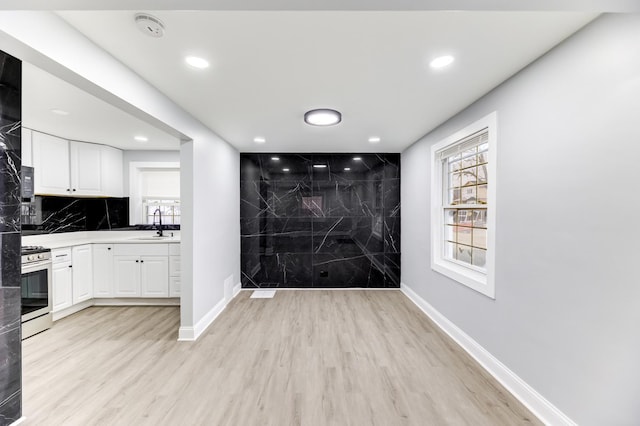 kitchen featuring light wood-type flooring, backsplash, gas stove, and white cabinets