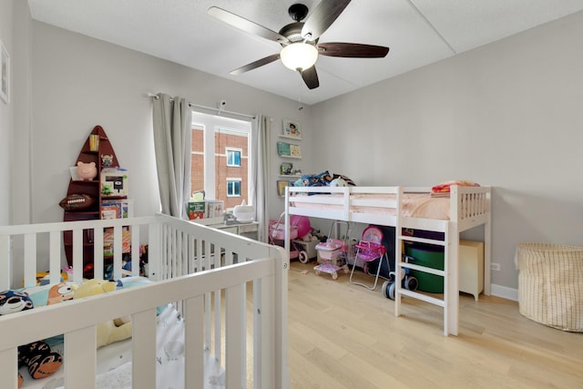 bedroom featuring a nursery area, wood finished floors, and a ceiling fan