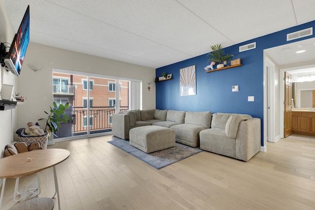 living area with light wood-type flooring, visible vents, and baseboards