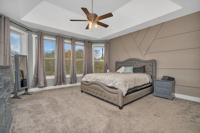 bedroom featuring ceiling fan, multiple windows, a raised ceiling, and carpet