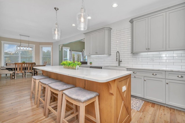 kitchen featuring a breakfast bar area, decorative light fixtures, a center island, gray cabinets, and sink