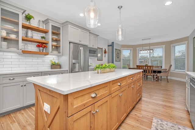 kitchen with appliances with stainless steel finishes, gray cabinetry, light stone counters, pendant lighting, and a center island