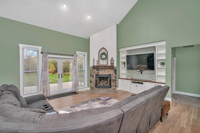 living room with high vaulted ceiling, a stone fireplace, french doors, and light hardwood / wood-style flooring