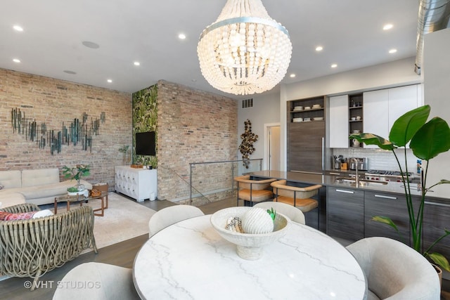 dining area with brick wall, dark wood-type flooring, and a notable chandelier