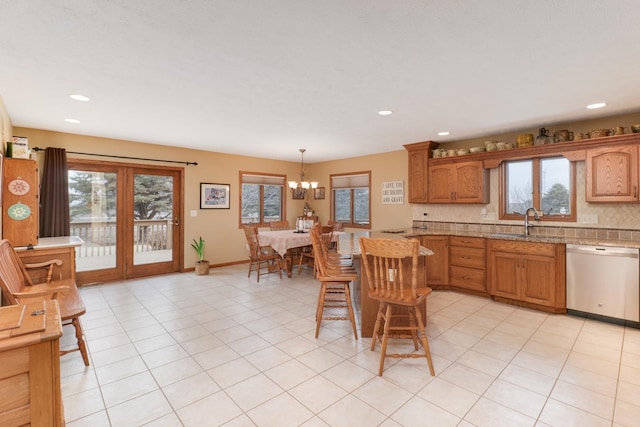 kitchen with plenty of natural light, dishwashing machine, brown cabinets, hanging light fixtures, and a sink