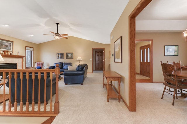 living area with ceiling fan, a tile fireplace, light colored carpet, baseboards, and vaulted ceiling