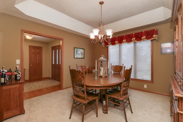 dining room with an inviting chandelier, baseboards, a tray ceiling, and light colored carpet