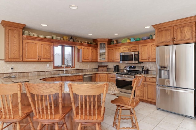 kitchen featuring appliances with stainless steel finishes, a sink, glass insert cabinets, and tasteful backsplash