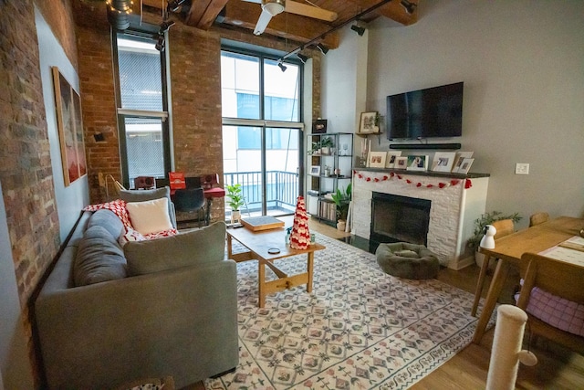 living area featuring a brick fireplace, a towering ceiling, brick wall, and wood finished floors