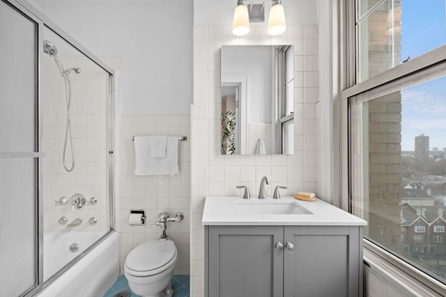 full bathroom with bath / shower combo with glass door, tile walls, vanity, and toilet