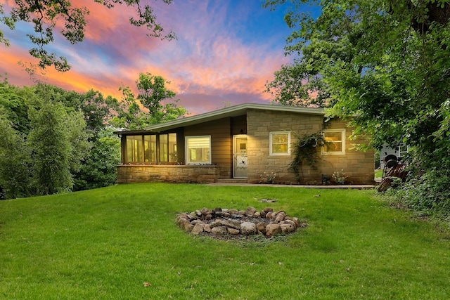 view of front facade featuring a sunroom, a lawn, and a fire pit