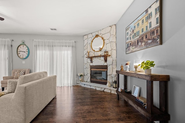 living room with a stone fireplace and dark hardwood / wood-style flooring