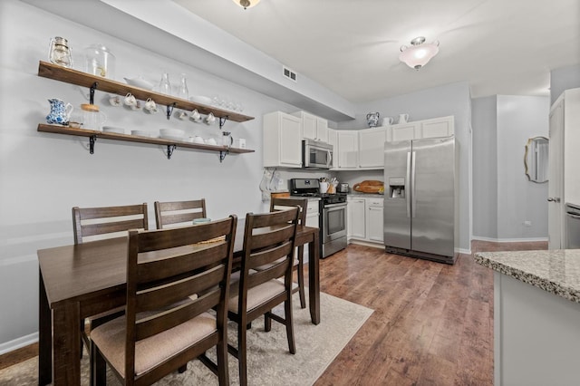 kitchen with white cabinetry, light stone counters, dark wood-type flooring, and stainless steel appliances