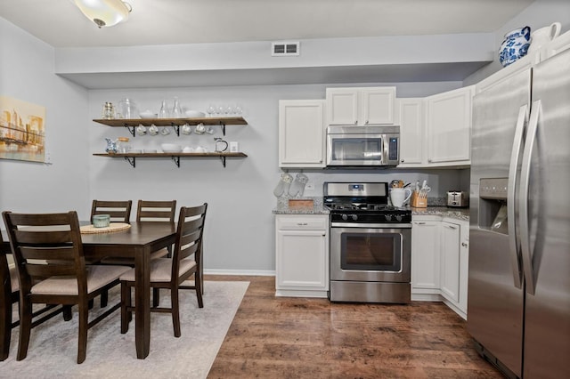 kitchen featuring white cabinetry, appliances with stainless steel finishes, light stone countertops, and dark wood-type flooring