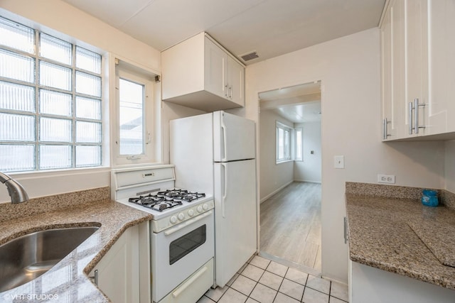 kitchen with sink, white gas range oven, light stone counters, white cabinets, and light tile patterned flooring