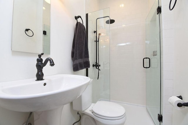 bathroom featuring sink, a shower with shower door, and toilet