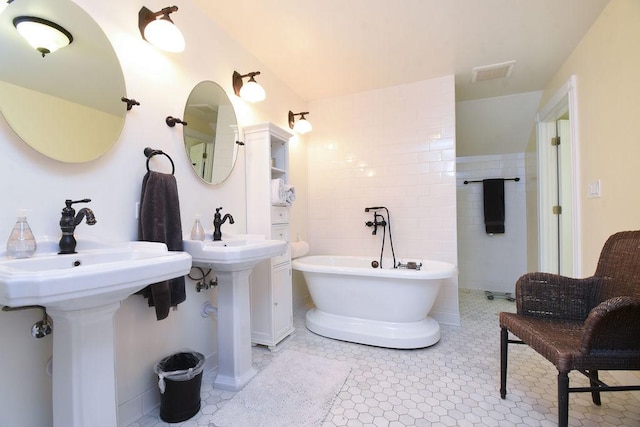 bathroom with a washtub, tile patterned flooring, tile walls, and dual sinks