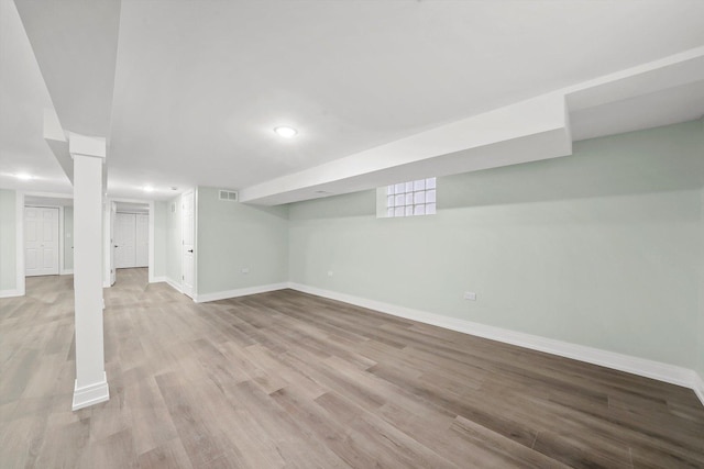 finished basement featuring visible vents, light wood-style flooring, and baseboards