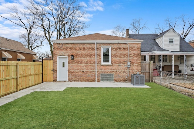 back of house featuring a fenced backyard, a lawn, cooling unit, and brick siding