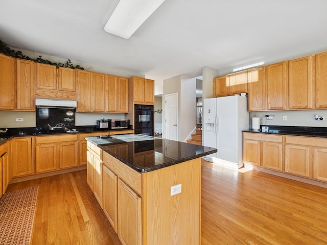 kitchen featuring white refrigerator with ice dispenser, double oven, a kitchen island, and light wood-type flooring