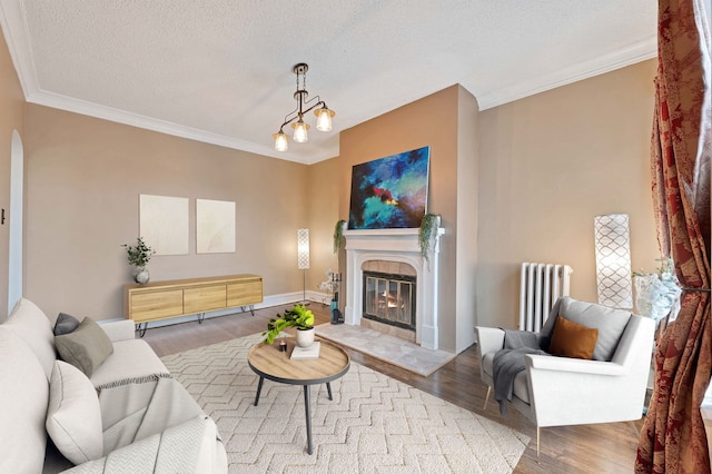 living room featuring radiator heating unit, hardwood / wood-style flooring, a tiled fireplace, crown molding, and a textured ceiling