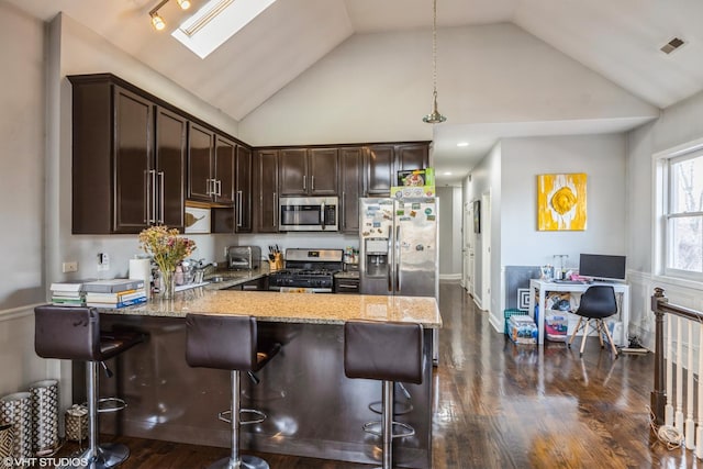 kitchen with pendant lighting, a kitchen bar, light stone counters, stainless steel appliances, and dark brown cabinets