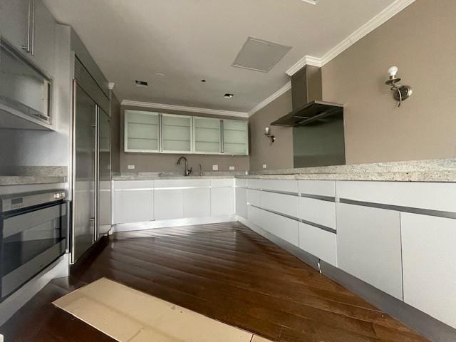 kitchen featuring white cabinetry, stainless steel oven, crown molding, and wall chimney range hood