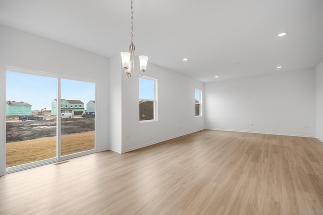 unfurnished room featuring a notable chandelier and light hardwood / wood-style flooring