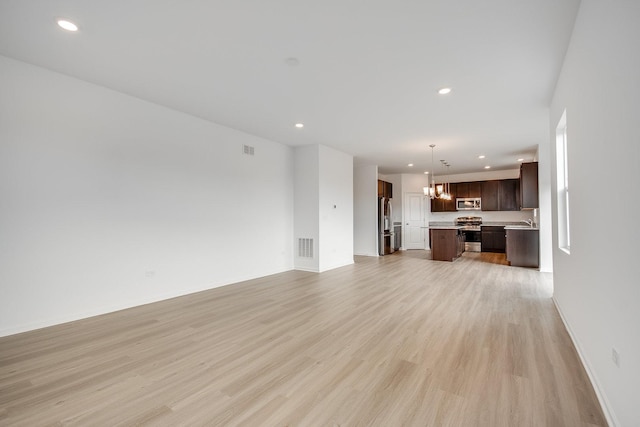 unfurnished living room featuring an inviting chandelier and light wood-type flooring