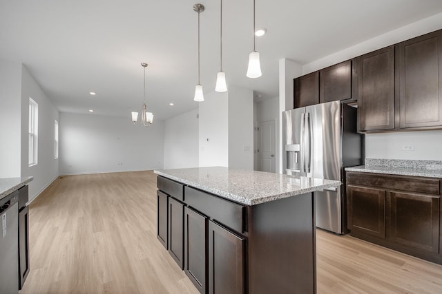 kitchen featuring appliances with stainless steel finishes, decorative light fixtures, a center island, light stone counters, and light hardwood / wood-style flooring