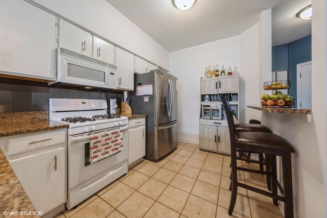 kitchen with light tile patterned floors, white appliances, dark stone counters, decorative backsplash, and white cabinets