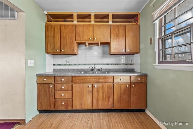 kitchen with a sink, open shelves, tasteful backsplash, brown cabinetry, and dark countertops