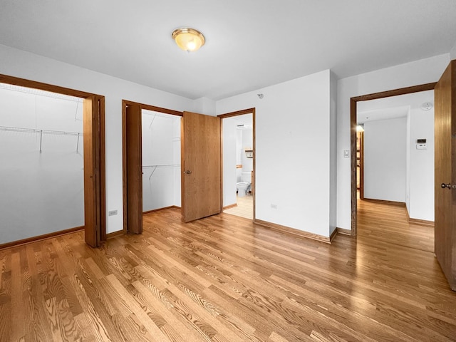 unfurnished bedroom featuring multiple closets, ensuite bathroom, and light hardwood / wood-style floors