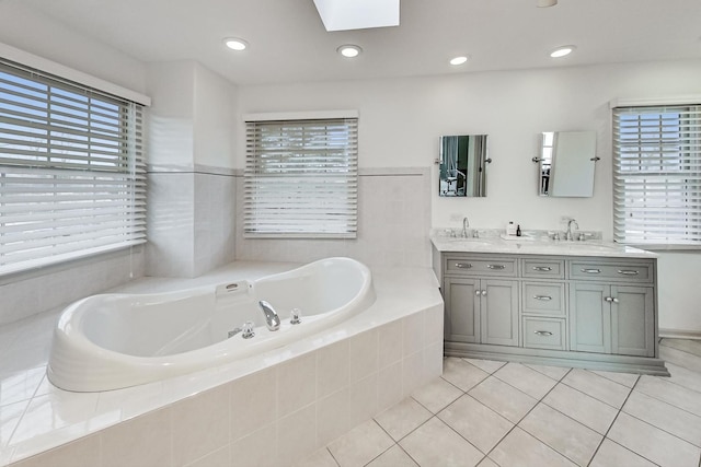 bathroom featuring vanity, a relaxing tiled tub, tile patterned floors, and a skylight