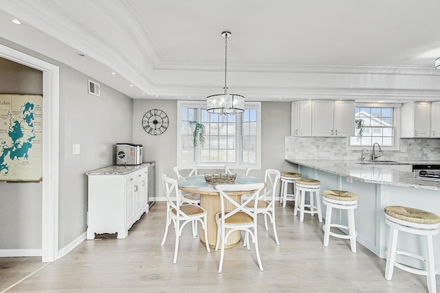 dining room with sink, light hardwood / wood-style flooring, an inviting chandelier, ornamental molding, and a raised ceiling