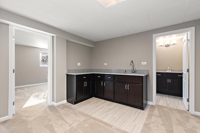 interior space with dark brown cabinetry, sink, light carpet, and a drop ceiling