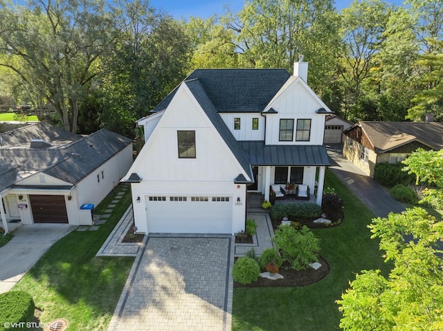 modern inspired farmhouse featuring metal roof, covered porch, a front yard, a standing seam roof, and a chimney