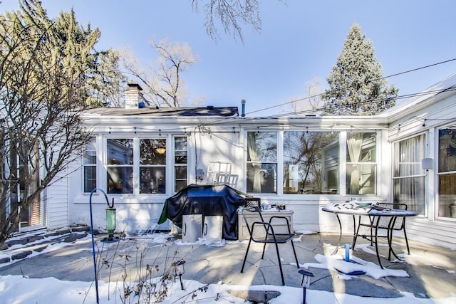 snow covered rear of property with a chimney and a patio