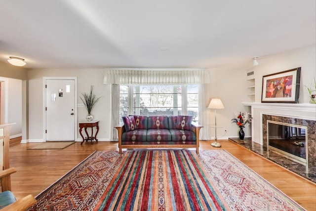 living area featuring built in shelves, a premium fireplace, baseboards, and wood finished floors