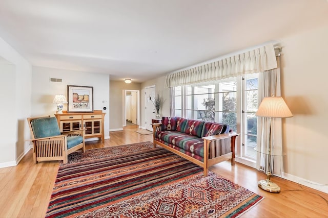 living area with light wood-type flooring, visible vents, and baseboards