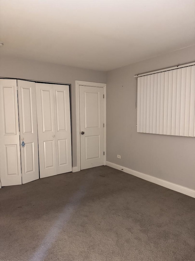 unfurnished bedroom featuring dark colored carpet, a closet, and baseboards