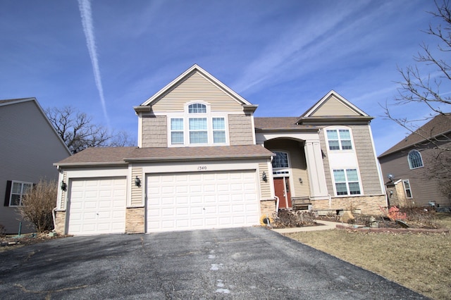 view of front of home featuring stone siding, driveway, and roof with shingles