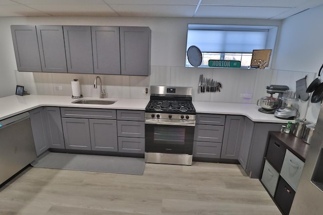 kitchen featuring sink, light hardwood / wood-style flooring, appliances with stainless steel finishes, gray cabinetry, and a drop ceiling