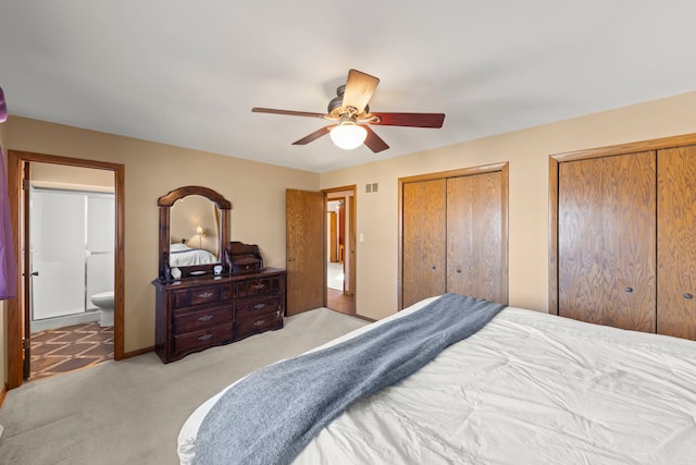 bedroom with light carpet, visible vents, a ceiling fan, ensuite bath, and two closets