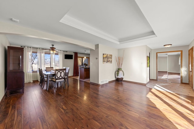 unfurnished dining area with visible vents, a ceiling fan, dark wood finished floors, baseboards, and a raised ceiling