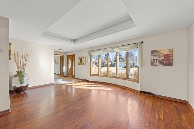 interior space with a tray ceiling, visible vents, baseboards, and wood finished floors