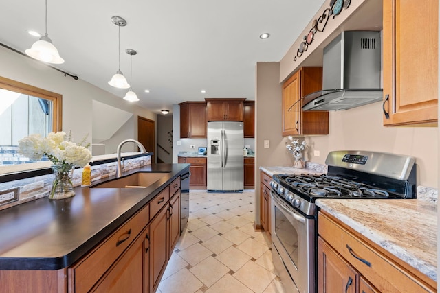 kitchen featuring pendant lighting, brown cabinets, stainless steel appliances, a sink, and wall chimney exhaust hood