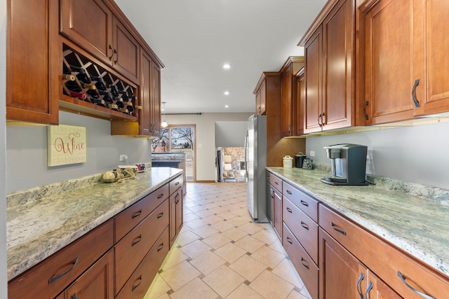 kitchen with brown cabinetry, freestanding refrigerator, recessed lighting, and light stone countertops