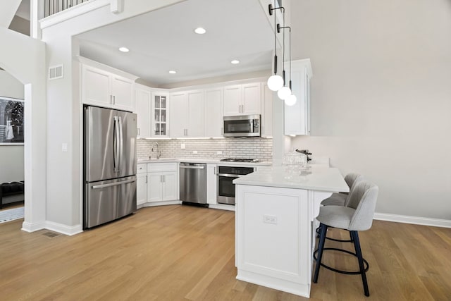 kitchen with appliances with stainless steel finishes, white cabinetry, hanging light fixtures, a kitchen breakfast bar, and tasteful backsplash